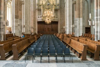 Grijze kunststof stoelen in rijen geplaatst in een kerkinterieur met houten kerkbanken en orgel op de achtergrond.