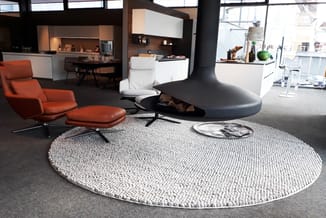 Moderne kantoorlounge met oranje relaxstoel, wit poef, zwarte hangende fireplace en ronde grijze getuft tapijt.