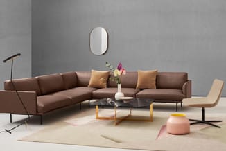 Bruine hoekbank met gele kussens, zwarte marmeren salontafel, beige loungefauteuil, staande lamp en ovale spiegel in minimali