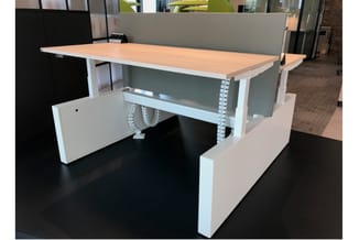 Elektrisch verstelbaar bureau met houten blad, witte onderstel en grijze akoestische scherm in modern kantoor.