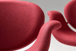 Rode stoelen met gebogen armsteunen en witte zitting, gemaakt van gestructureerde stof, tegen grijze achtergrond.