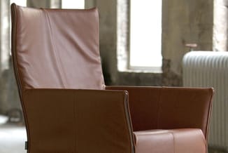 Bruine lederen loungestoel met hoge rugleuning in industriële ruimte met betonnen wanden en raam.