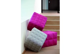 Roze en grijze gequilte poef-elementen tegen witte wand in houten interieur.