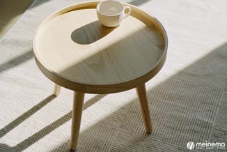 Ronde houten bijzettafel met licht fineer, drie poten, met beige mok erop, op neutrale gestructureerde vloerbedekking in mini