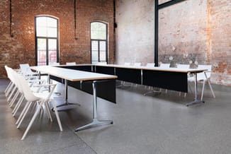 Moderne vergaderzaal met U-vormige zwarte vergadertafel, witte stoelen, bakstenen muren en grote ramen.
