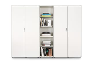 Witte schuifkastenwand met centrale open boekenkast, gevuld met boeken en kantooraccessoires.