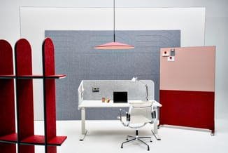 Werkplek met wit bureau, witte bureaustoel, grijze akoestische wandpanelen, rode fluwelen scheidingswanden, roze hangende lam