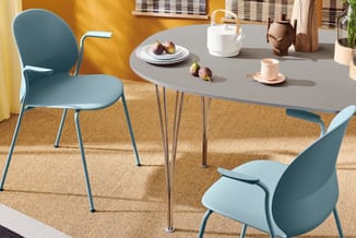 Moderne eettafel met grijsblad en metalen poten, omgeven door drie blauwe stoelen op beige tapijt in geel interieur.