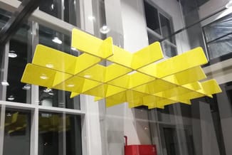 Gele akoestische plafondpanelen in zigzagvorm opgehangen in moderne kantoorruimte met glazen wanden.