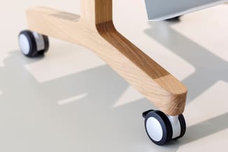 Houten bureaustoel met lichte houten rugleuning en zwartwitte wielen, geplaatst in een modern kantoor met monitoren.