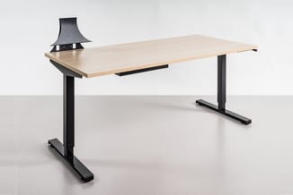 Zit-stabureau met licht houten blad en zwart metalen onderstel, voorzien van een zwarte bureaulamp, tegen witte achtergrond.