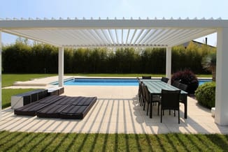 Moderne terrasoverkapping met witte aluminium frame boven lounge- en eettuin met zwarte stoelen, tafel en ligbed bij zwembad.