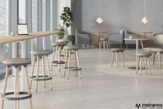 Modern kantoor met houten bartafel, groene en grijze barkrukken, grijze fauteuils, verlichtingsarmaturen en plant tegen raamw