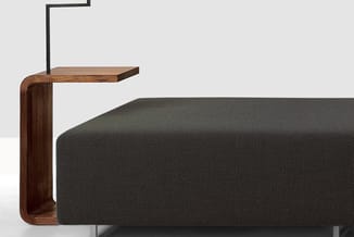 Houten bedframe met donkergrijs linnen bekleding en integraal nachtkastje met metalen leeslamp.
