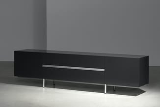 Zwart TV-meubel met grijze metalen handgreep en zilverkleurige poten op lichte betonvloer tegen grijze wand.