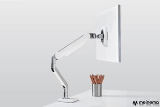Wit monitorarm met ergonomische beugel op witte bureaustandaard, naast zilveren beker met pennen op wit bureau.
