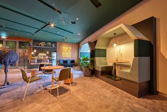 Modern kantoor met turquoise plafond, bruin linoleum, ronde houten tafel, beige stoelen, groene lounge-module en verlichte ni