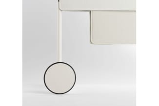 Beige stofkussen op zwart frame aan witte poot, onderdeel van modulair zitmeubel in minimalistische setting.