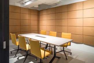 Moderne vergaderruimte met lange witte tafel, gele bureaustoelen met zwart onderstel, bruine akoestische wandpanelen en LED-p