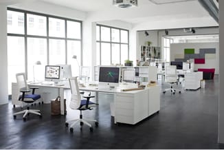 Modern open kantoor met witte bureaus, ergonomische stoelen met blauwe zittingen, computermonitors, opbergkasten en kleurrijk