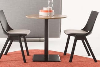 Ronde tafel met zwart onderstel en houten blad, twee zwarte stoelen met beige zitting op oranje tapijt in kantooromgeving.