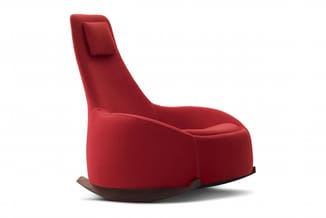 Rood gestoffeerde schommelstoel met hoge rugleuning, geïntegreerde neksteun en donker houten schommelbasis, tegen witte achte