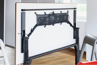 Zwart ergonomisch kabelorganisatiesysteem onder bureaus, gemonteerd aan witte whiteboard met houten frame.