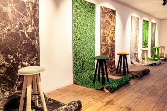 Showroom met houten vloer, grijze barkrukken met zwarte poten, en wandbekleding in groen en bruintinten met grafische patrone