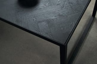 Zwarte vergadertafel met houtnerf-blad en stalen poten, gedeeltelijk zichtbaar in grijze ruimte.