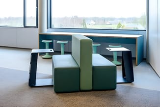 Modulaire zitgroep met groene en grijze elementen in moderne kantoorruimte met grote ramen en uitzicht.