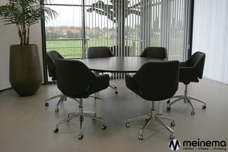 Moderne vergaderruimte met zwarte conferentietafel, zwarte bureautoelen op wielen, potplant en verticale jaloezieën met groen