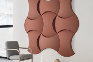 Terracottakleurige wandpanelen met organische bolle vormen naast grijze fauteuil in moderne kantoorruimte.