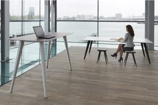 Moderne kantoorruimte met houten vloer, twee grijze werktafels met metalen poten, zwarte kruk, laptop, uitzicht op water en s