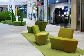 Groene modulaire zitmodules in een winkelpassage met detailwinkels op de achtergrond.