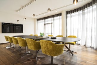 Moderne vergadertafel met zwart blad en zwarte onderstel, omgeven door gele gestoffeerde stoelen met metalen poten in ruime k