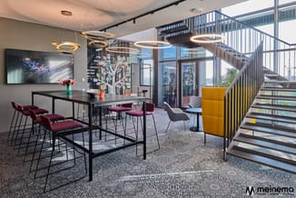 Modern kantoor met zwarte tafel, bordeauxrode en grijze stoelen, gouden hangende verlichting, trappen met gele accenten en gr