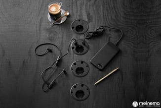 Overhead view op donkergrijs houten bureau met koffiekopje, in-ear headphones, vier zwarte speakercones, stroomadapter en gou