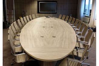 Ronde vergadertafel in licht hout met zilveren onderstel, omgeven door beige stoelen met chromé frame in moderne vergaderruim