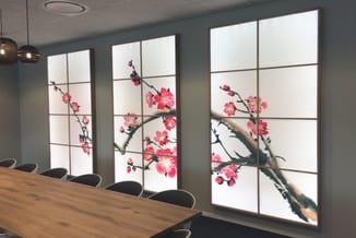 Vergaderruimte met verlichte panelen met bloemenprint, houten vergadertafel en zwarte bureaisstoelen.
