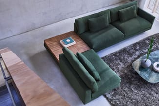 Groene zitgroep met hoekopstelling en houten salontafel met boek en decoratief object, op grijze vloer met tapijt.