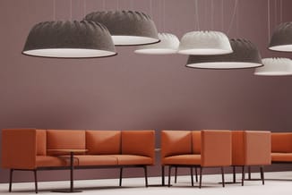 Kantoorinterieur met oranje modulaire zitgroep, grijze en witte hangende akoestische lampen tegen roze wand.