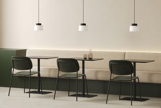Moderne kantinehoek met drie zwarte stoelen aan kleine zwarte tafels, beige loungebank achter, drie hangende wit-zwarte pende