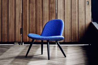Blauwe loungestoel met structuurstof op zwarte poten, staande op houten vloer voor houten wandpanelen.