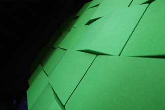 Groen akoestisch wandpaneel met driedimensionaal reliëfpatroon, gefotografeerd tegen donkere achtergrond.