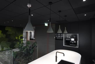 Moderne keuken met wit keukeneiland, zwarte hangende kegellampen, zwarte afzuigkap, ingebouwde apparatuur en groen wandbegroe