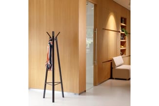 Zwarte garderobe-standaard met driepotige vorm tegen lichte houten wand in moderne kantooromgeving met loungebank.