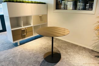 Ronde tafel met zwart onderstel en houten blad in moderne kantooromgeving, naast witte kasten met glazen deuren.