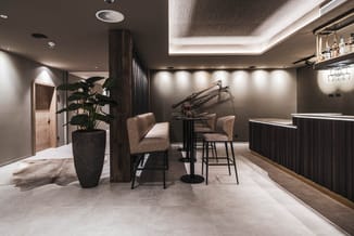 Moderne kantoorlounge met grijze barkrukken aan zwarte bartafel, donkerhouten scheidingswand, potplant in betonnen pot, fiets