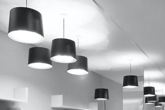 Zwarte hangende design lampen met witte lichtscherming in moderne kantoorruimte met wit plafond.