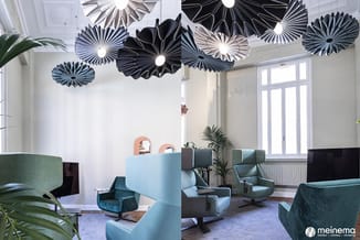 Modern kantoor met blauwe en groene fauteuils, zwarte plafondpanelen, grote ramen, planten en minimalistisch design.